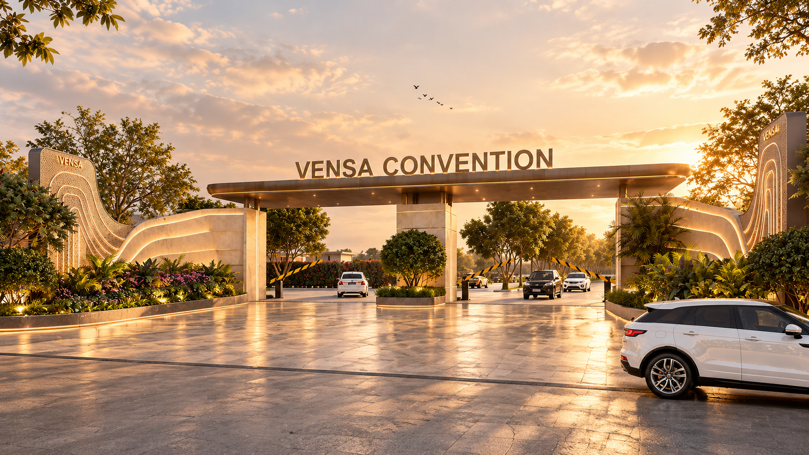 The Vensa Convention entrance gate at golden hour: the lit canopy with the name across it, curved stone walls and planting either side, cars on the drive